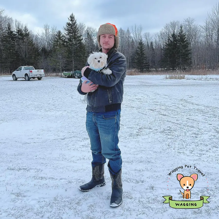 A man holding a small dog in a snowy field